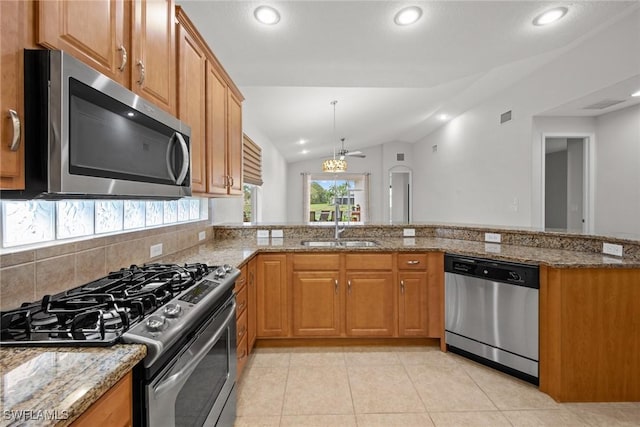 kitchen featuring lofted ceiling, light stone counters, a sink, appliances with stainless steel finishes, and brown cabinets