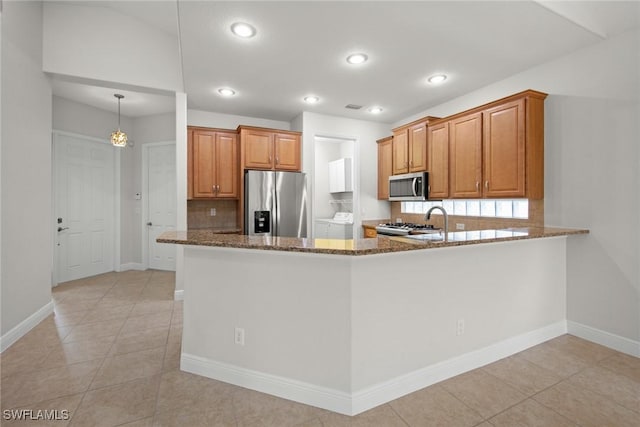 kitchen with stainless steel appliances, dark stone countertops, a peninsula, and brown cabinets