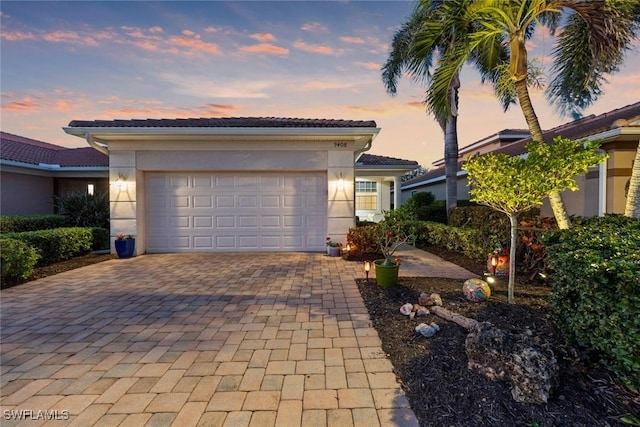 view of front of house featuring an attached garage, a tiled roof, decorative driveway, and stucco siding