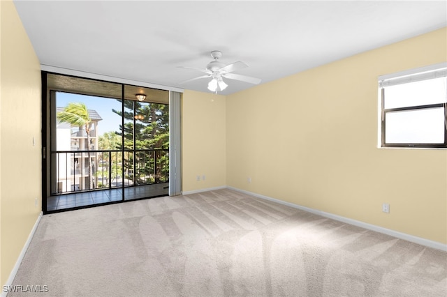 carpeted empty room featuring ceiling fan, a healthy amount of sunlight, and a wall of windows