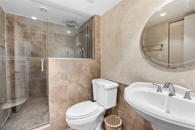 bathroom with tile walls, sink, a shower with shower door, and toilet