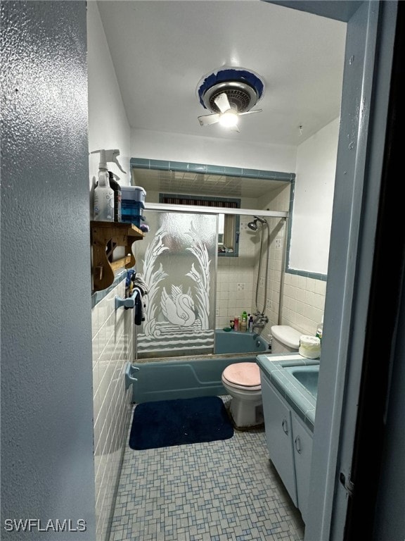 full bathroom with toilet, vanity, bath / shower combo with glass door, and tile walls