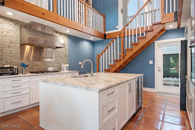 kitchen featuring white cabinets, sink, wall chimney exhaust hood, and a center island with sink