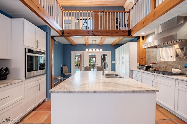 kitchen featuring sink, a kitchen island with sink, stainless steel appliances, white cabinets, and wall chimney exhaust hood