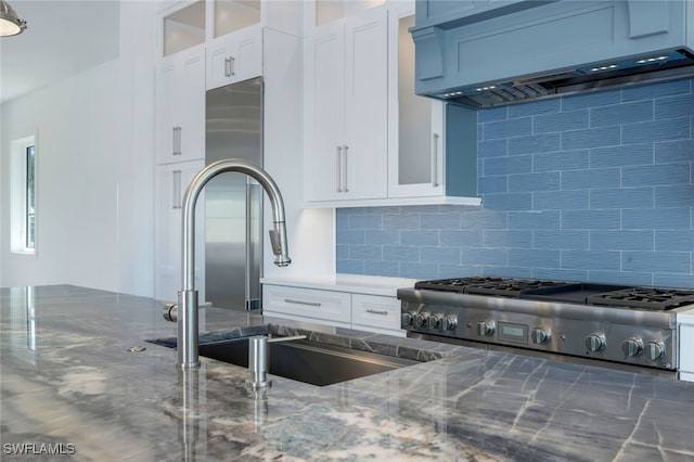 kitchen with tasteful backsplash, sink, white cabinets, dark stone counters, and custom range hood