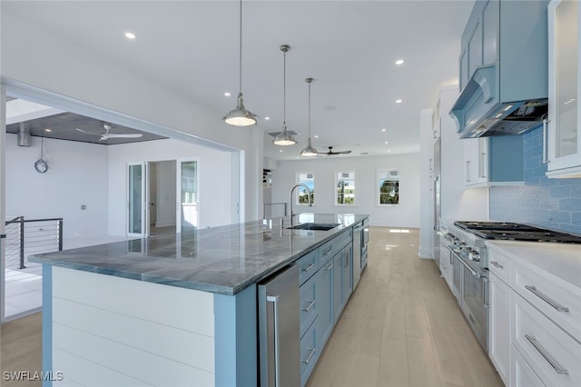 kitchen with decorative light fixtures, tasteful backsplash, sink, white cabinets, and a large island with sink