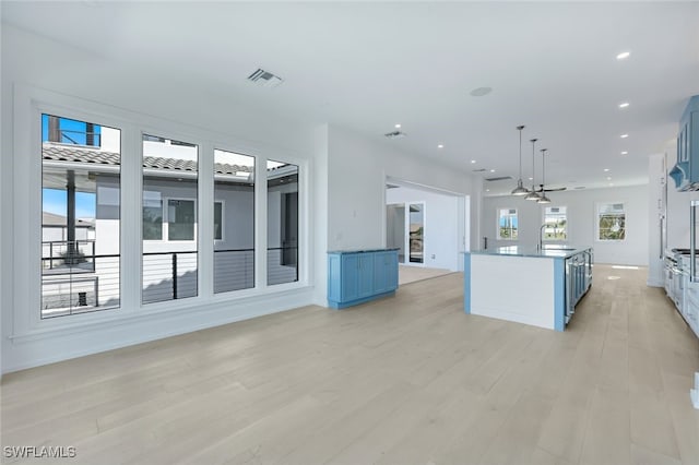 kitchen with blue cabinetry, sink, a center island, pendant lighting, and light hardwood / wood-style floors