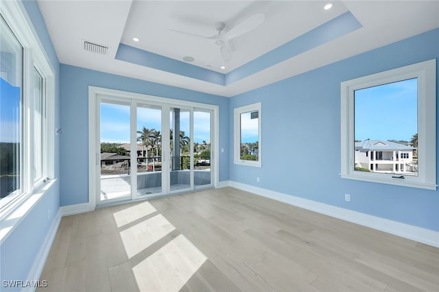 empty room featuring ceiling fan, plenty of natural light, light hardwood / wood-style floors, and a tray ceiling