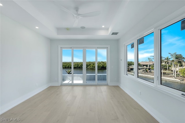 unfurnished room with ceiling fan, a tray ceiling, and light hardwood / wood-style floors