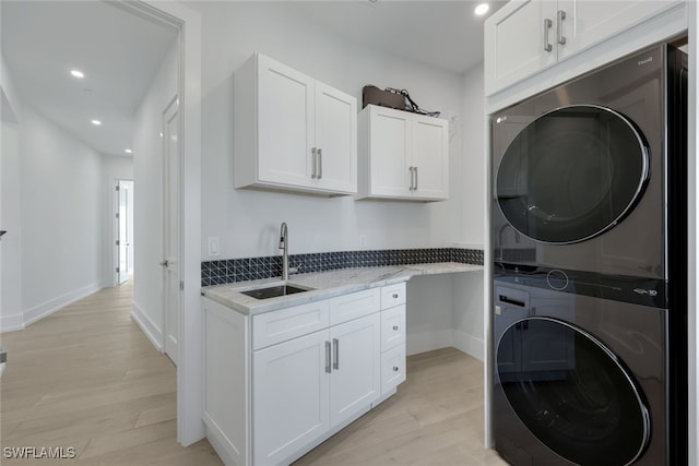 laundry area featuring cabinets, stacked washer / drying machine, light hardwood / wood-style floors, and sink