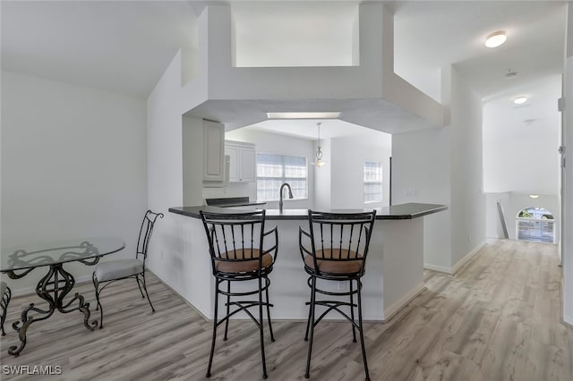 kitchen featuring decorative light fixtures, a breakfast bar area, light hardwood / wood-style floors, and kitchen peninsula