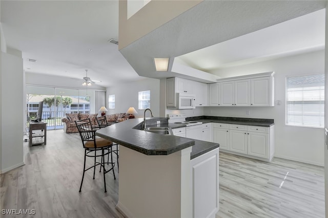 kitchen featuring white appliances, light hardwood / wood-style flooring, a breakfast bar, white cabinets, and kitchen peninsula