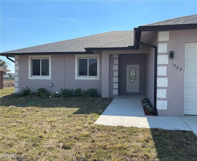 view of exterior entry featuring a garage and a lawn