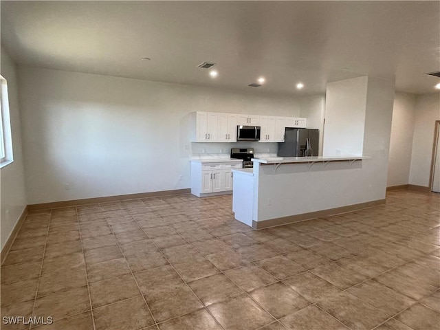 kitchen featuring stainless steel appliances, a kitchen bar, kitchen peninsula, and white cabinets