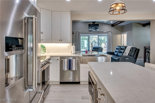 kitchen featuring white cabinetry, high end appliances, light stone countertops, and sink