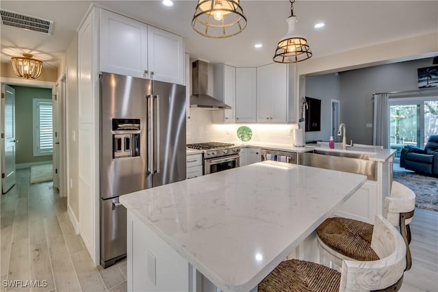 kitchen featuring wall chimney exhaust hood, white cabinetry, hanging light fixtures, premium appliances, and kitchen peninsula