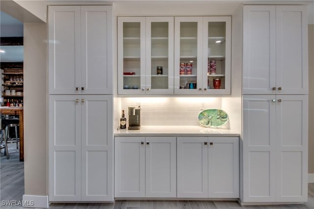 bar with white cabinetry, backsplash, and light wood-type flooring