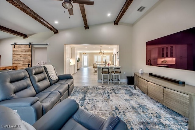 living room with vaulted ceiling with beams, light hardwood / wood-style floors, a barn door, and ceiling fan