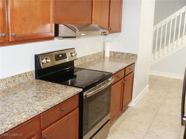 kitchen with wall chimney range hood, light tile patterned floors, light stone countertops, and stainless steel electric range oven