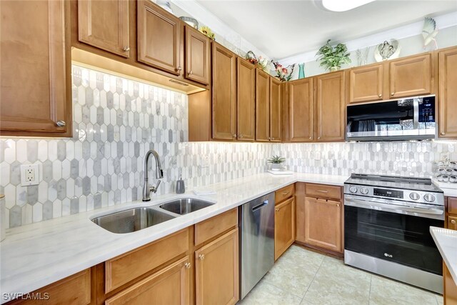 kitchen with appliances with stainless steel finishes, light stone countertops, backsplash, light tile patterned floors, and sink