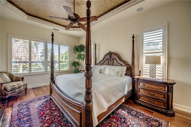 bedroom with ceiling fan, a tray ceiling, and hardwood / wood-style floors