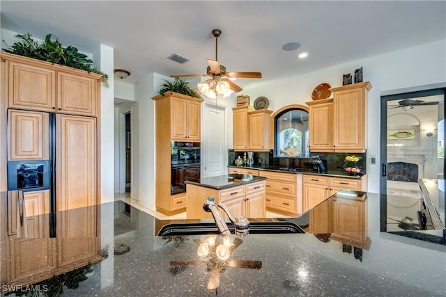 kitchen featuring sink, light brown cabinets, ceiling fan, dark stone counters, and decorative backsplash