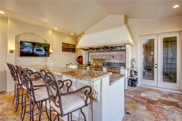 kitchen with premium range hood, a kitchen breakfast bar, kitchen peninsula, and light stone countertops