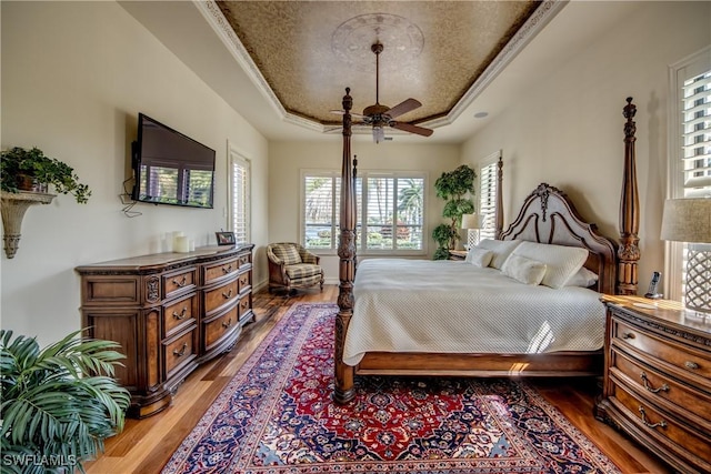 bedroom with hardwood / wood-style floors, a tray ceiling, ornamental molding, and ceiling fan