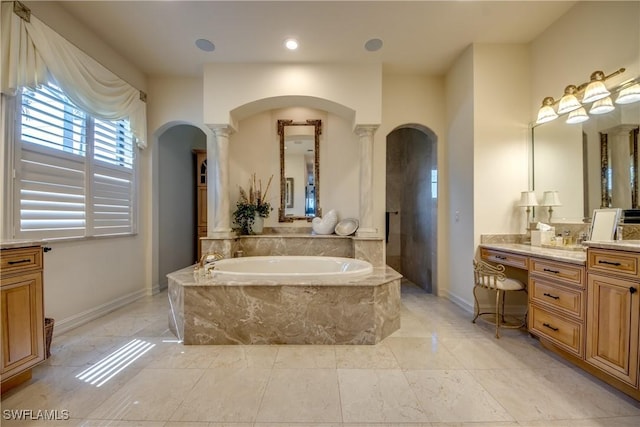 bathroom featuring decorative columns, vanity, and a relaxing tiled tub