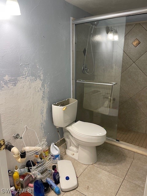 bathroom with a shower with door, tile patterned flooring, and toilet