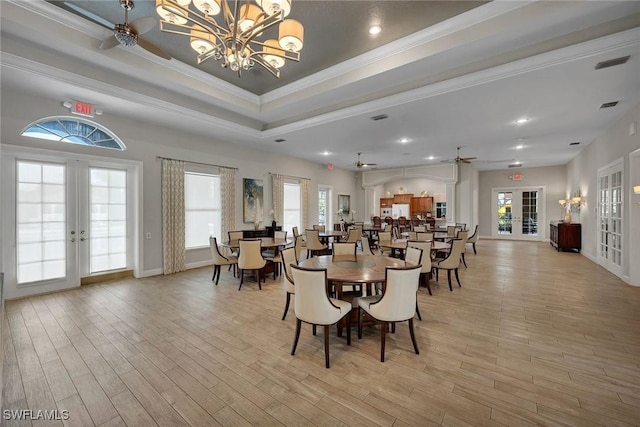 dining space featuring ceiling fan with notable chandelier, light hardwood / wood-style flooring, french doors, and a raised ceiling