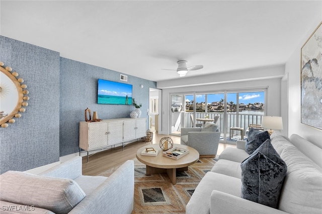 living room featuring visible vents, a ceiling fan, wood finished floors, wallpapered walls, and an accent wall