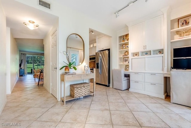 kitchen with appliances with stainless steel finishes, built in desk, white cabinets, and light tile patterned floors