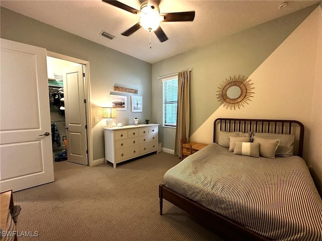 bedroom with a walk in closet, light colored carpet, visible vents, ceiling fan, and baseboards