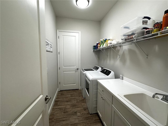 washroom with dark wood finished floors, washing machine and clothes dryer, cabinet space, a sink, and baseboards