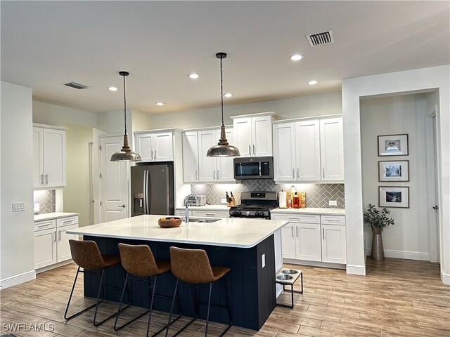 kitchen with a kitchen bar, sink, white cabinetry, a center island with sink, and appliances with stainless steel finishes