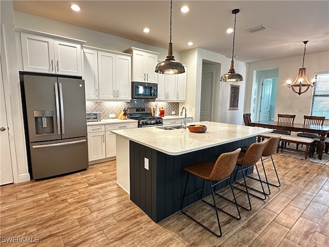 kitchen with white cabinetry, a kitchen island with sink, stainless steel appliances, and hanging light fixtures