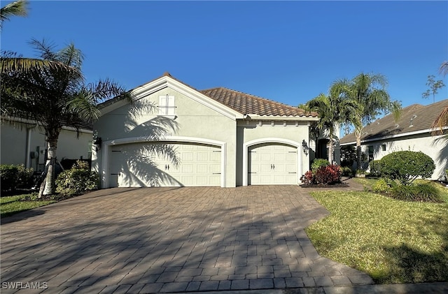 mediterranean / spanish-style house with a garage, a tiled roof, decorative driveway, and stucco siding