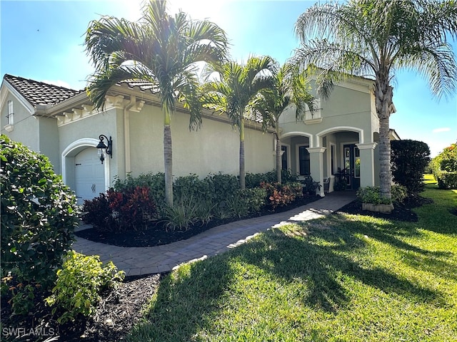 view of front facade with a garage, a tile roof, a front lawn, and stucco siding