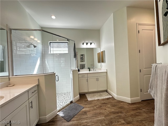 bathroom with a sink, two vanities, wood finished floors, baseboards, and a stall shower