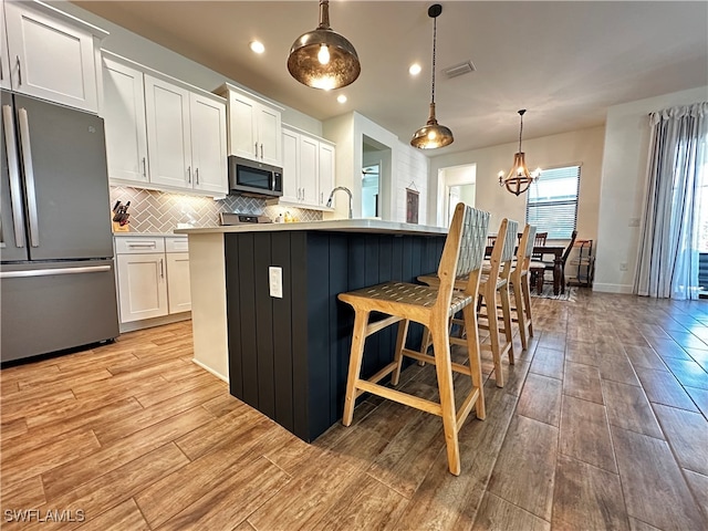 kitchen featuring appliances with stainless steel finishes, white cabinets, light wood-style flooring, and tasteful backsplash