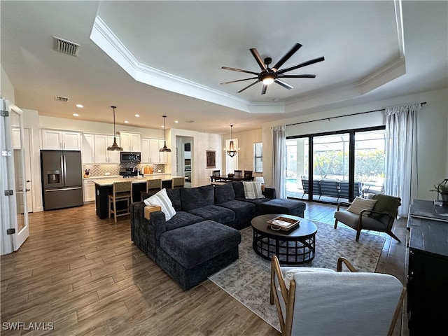 living area with ceiling fan, a tray ceiling, dark wood-type flooring, and visible vents