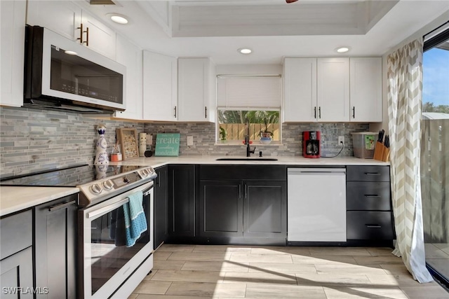 kitchen with sink, dishwasher, white cabinetry, electric range, and a tray ceiling