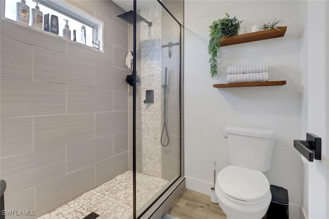 bathroom with wood-type flooring, toilet, and a tile shower