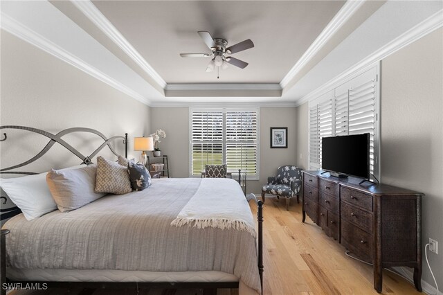 bedroom featuring ornamental molding, ceiling fan, light wood-type flooring, and a tray ceiling