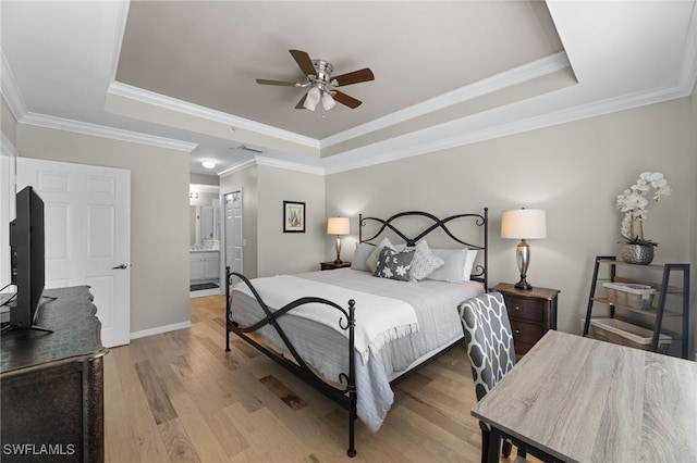 bedroom featuring ornamental molding, a tray ceiling, light hardwood / wood-style flooring, and ensuite bath