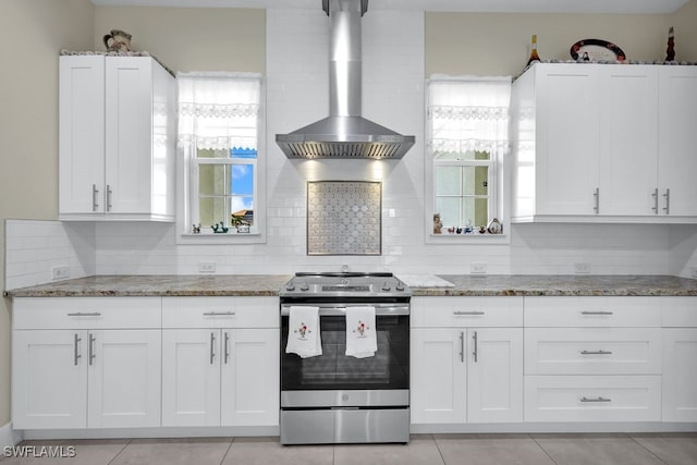 kitchen with wall chimney exhaust hood, stainless steel range with electric cooktop, stone countertops, decorative backsplash, and white cabinets