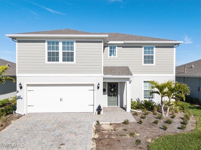 traditional home featuring roof with shingles, decorative driveway, an attached garage, and stucco siding