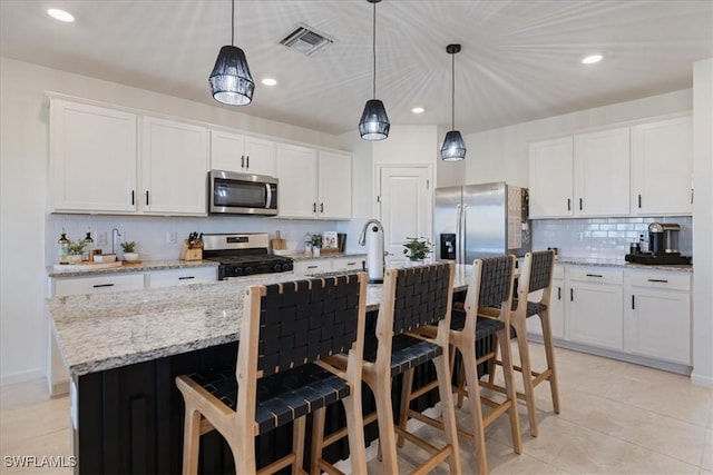 kitchen featuring hanging light fixtures, appliances with stainless steel finishes, an island with sink, decorative backsplash, and white cabinets