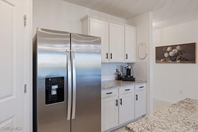 kitchen with white cabinetry, stainless steel fridge, light stone countertops, and backsplash